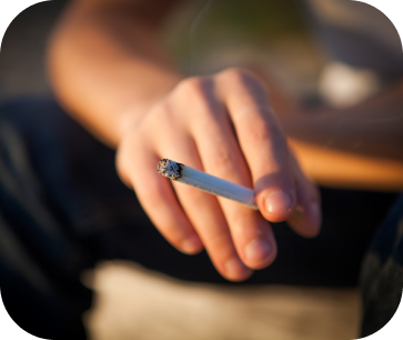 A hand holding a lit cigarette, with smoke visible.