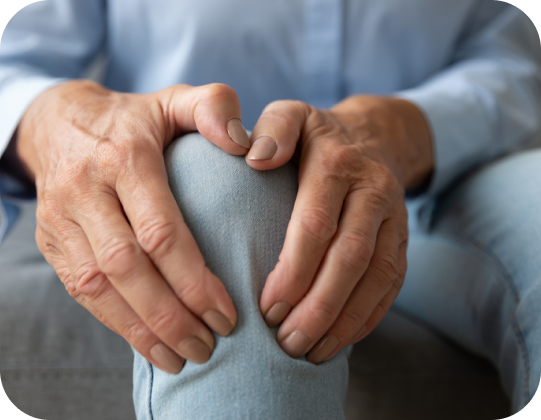 A person's hands rubbing a sore knee, indicating pain or discomfort associated with osteoarthritis.