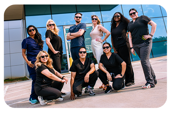 group of nine people posing together outside a modern building with glass windows