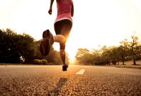 A Woman in athletic clothing runs down a paved road at sunset.