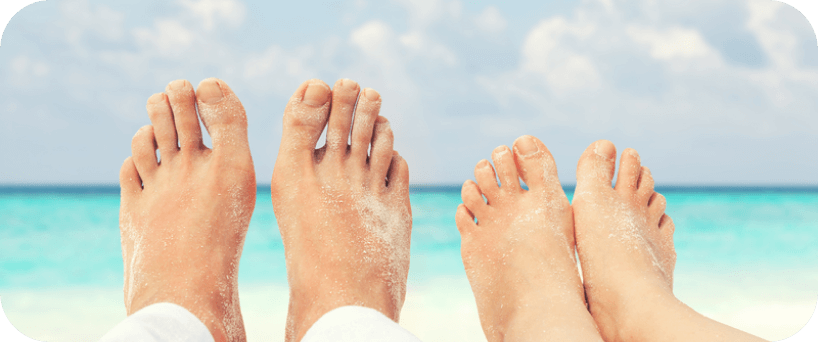 Sandy feet on a beach with the ocean in the background