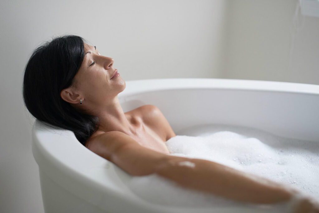 A mature woman relaxing in a bathtub, seeking relief from discomfort associated with Restless Legs Syndrome