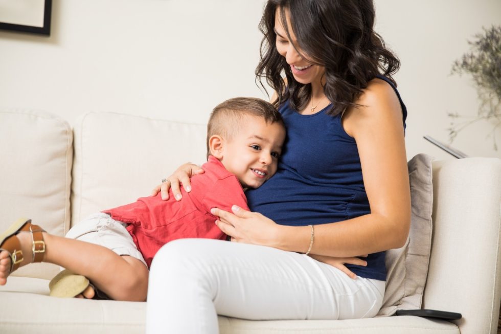 Cute little boy showing love towards unborn baby in mother's tummy at home