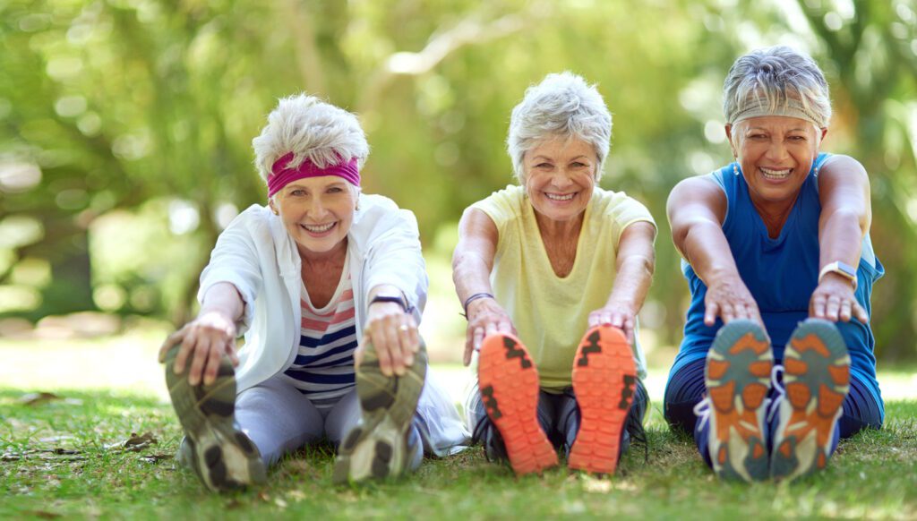 Three elderly ladies are smiling while exercising.