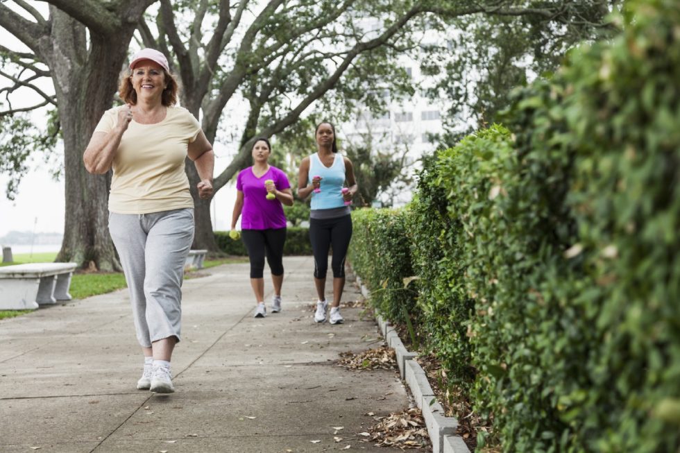 Multi-ethnic women exercising in park, power walking. Focus on senior woman (60s) in foreground.