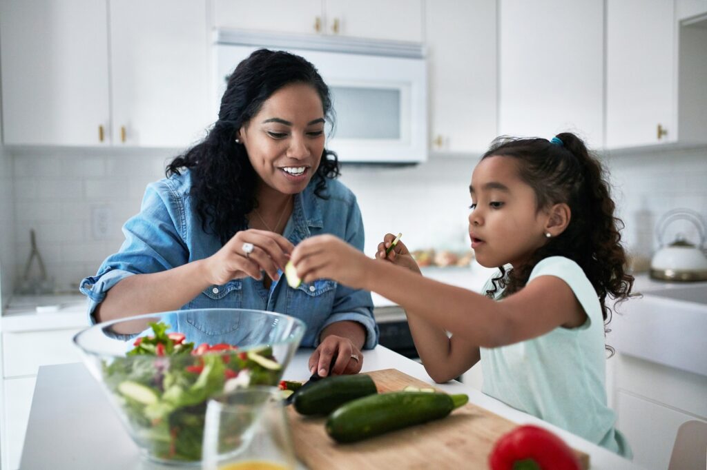 Mother and daughter preparing meal at home. Girl is learning to prepare food from woman. They are in kitchen.