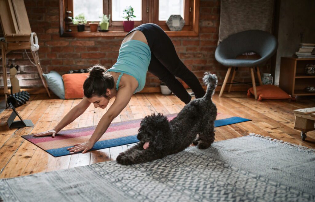 Woman practicing yoga with her dog, using the Downward Dog pose to improve leg circulation