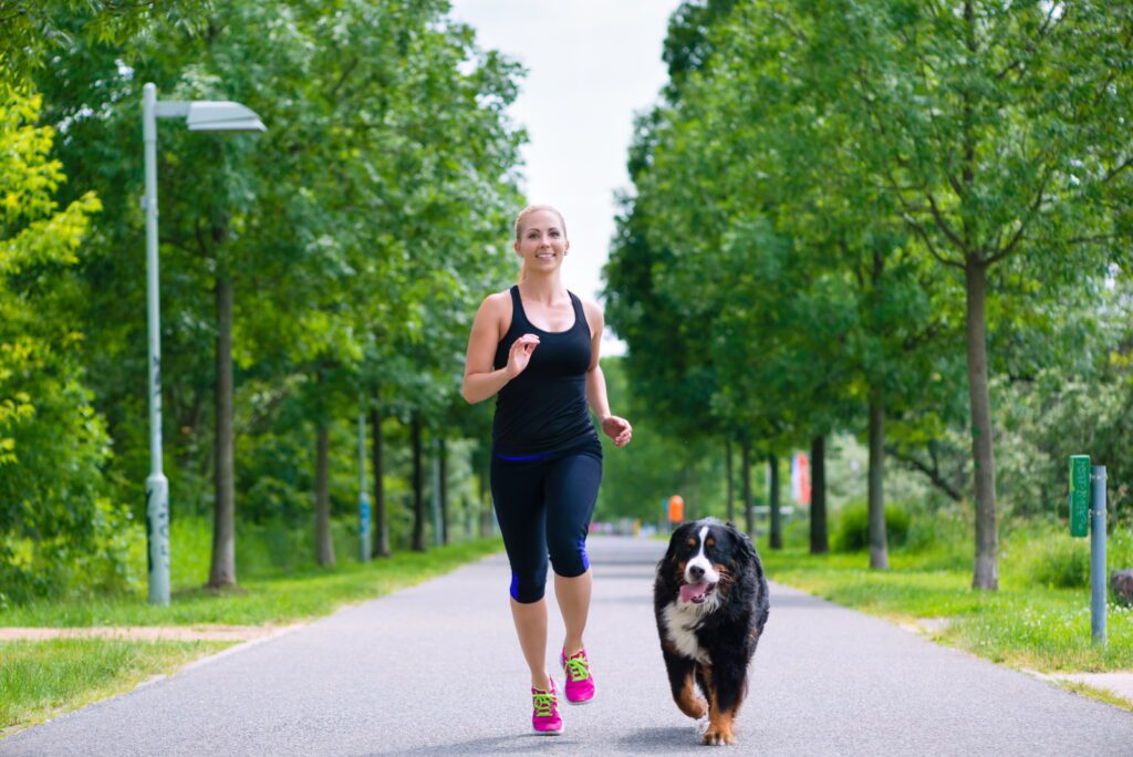 Urban sports - woman running for better fitness together with her dog in the city park on a cloudy summer day