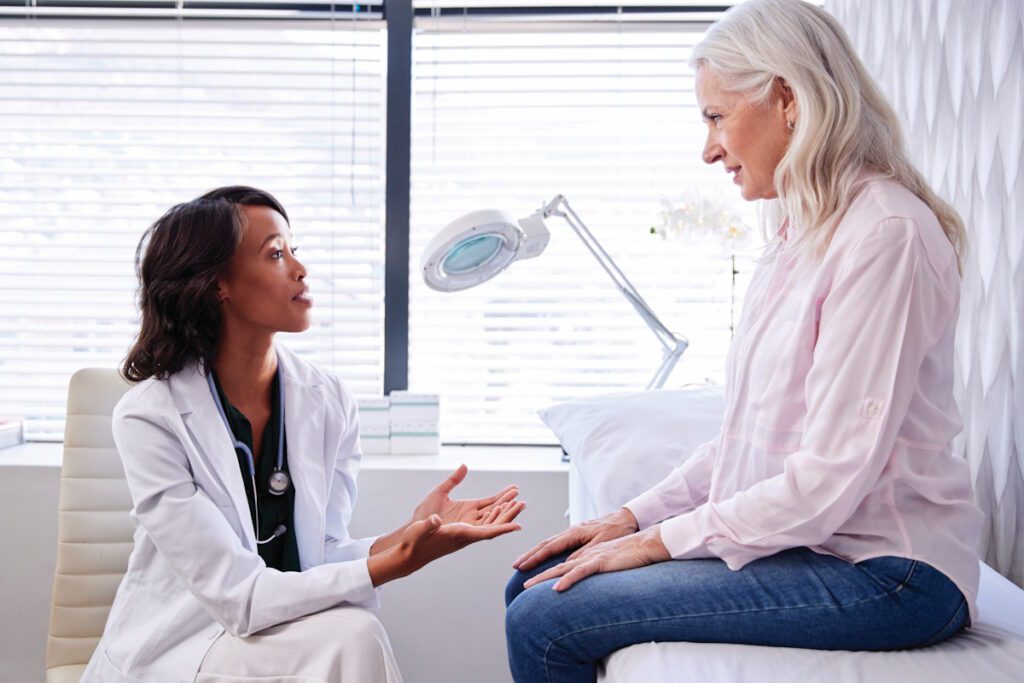 Mature Woman In Consultation With Female Doctor Sitting On Examination Couch In Office