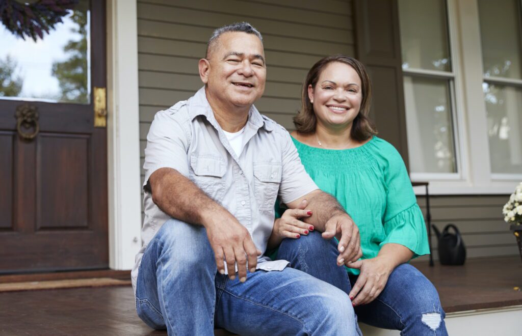 Portrait Of Smiling Senior Couple Sitting In Front Of Their Home