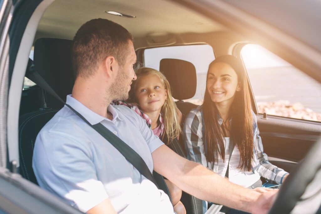 Happy family on a road trip in their car. Dad, mom and daughter are traveling by the sea or the ocean or the river. Summer ride by automobile.