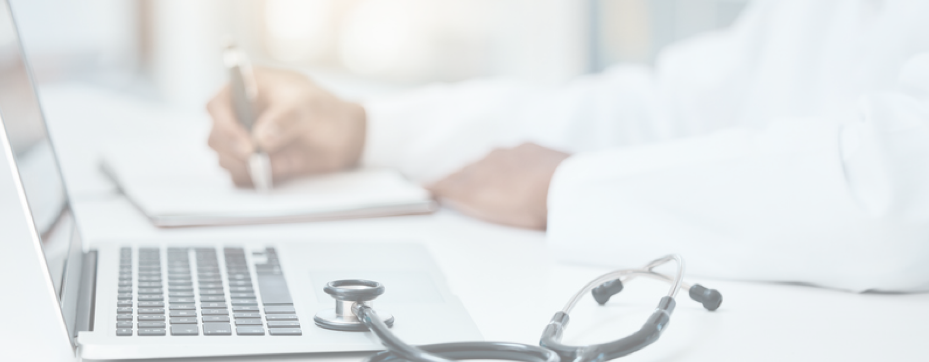 Doctor writing while placing his stethoscope on the laptop